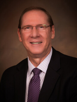 Headshot of Eric Eddings in a black suit, a purple tie, and a lilac dress shirt