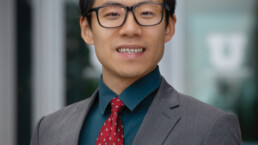 Chauncheng Duan in grey suit and tie wearing glasses and smiling.